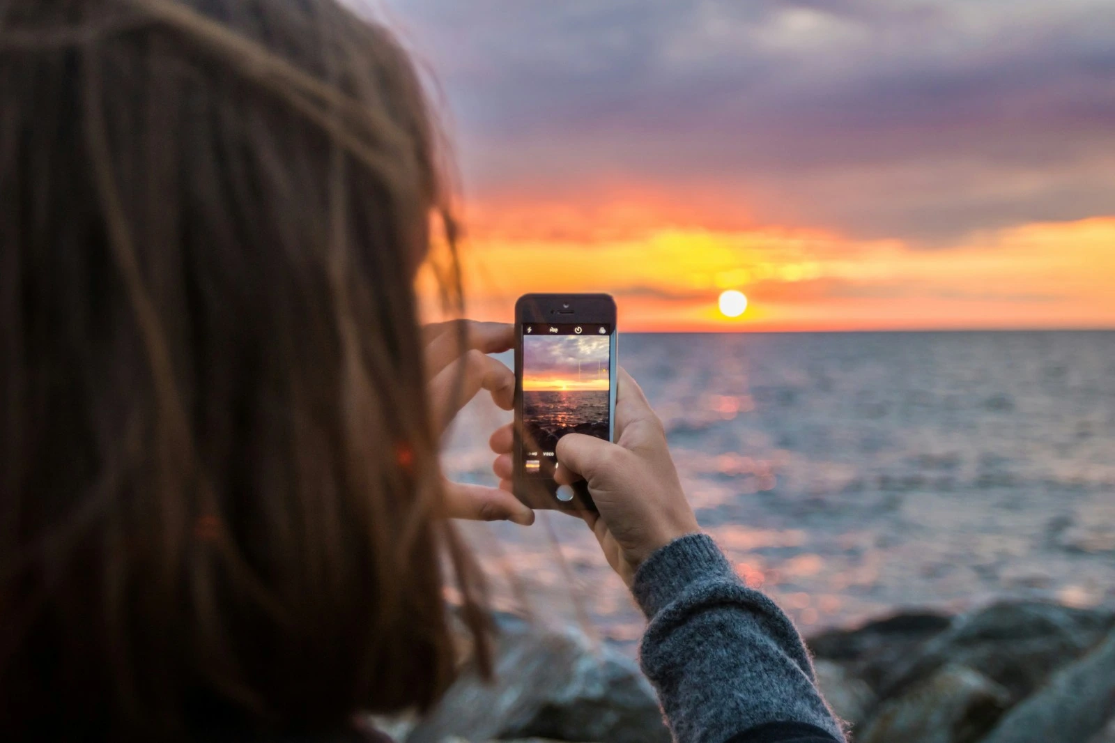 Osoba mobitelom fotografira zalazak sunca